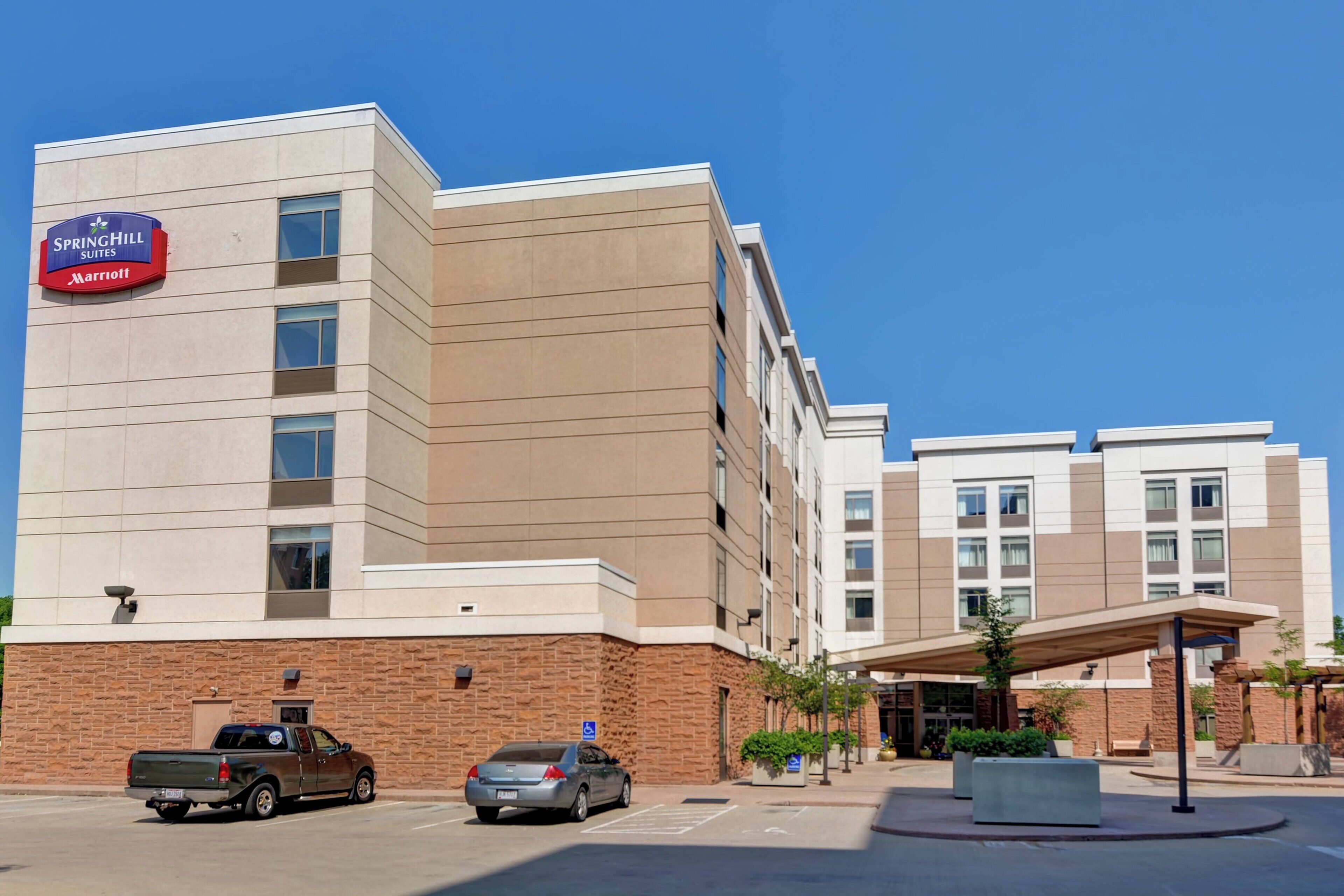 Un hotel SpringHill Suites Marriott con fachada de ladrillo, varios espacios de estacionamiento y un área de acceso cubierta.