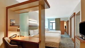 Une chambre d’hôtel équipée d’un bureau, d’une chaise, de deux lits, d’une télévision et d’une salle de bain visible à travers une paroi en verre.