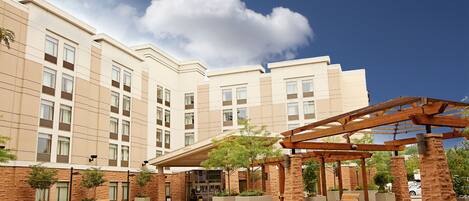 A hotel with a covered outdoor area, planters, and a clear sky.