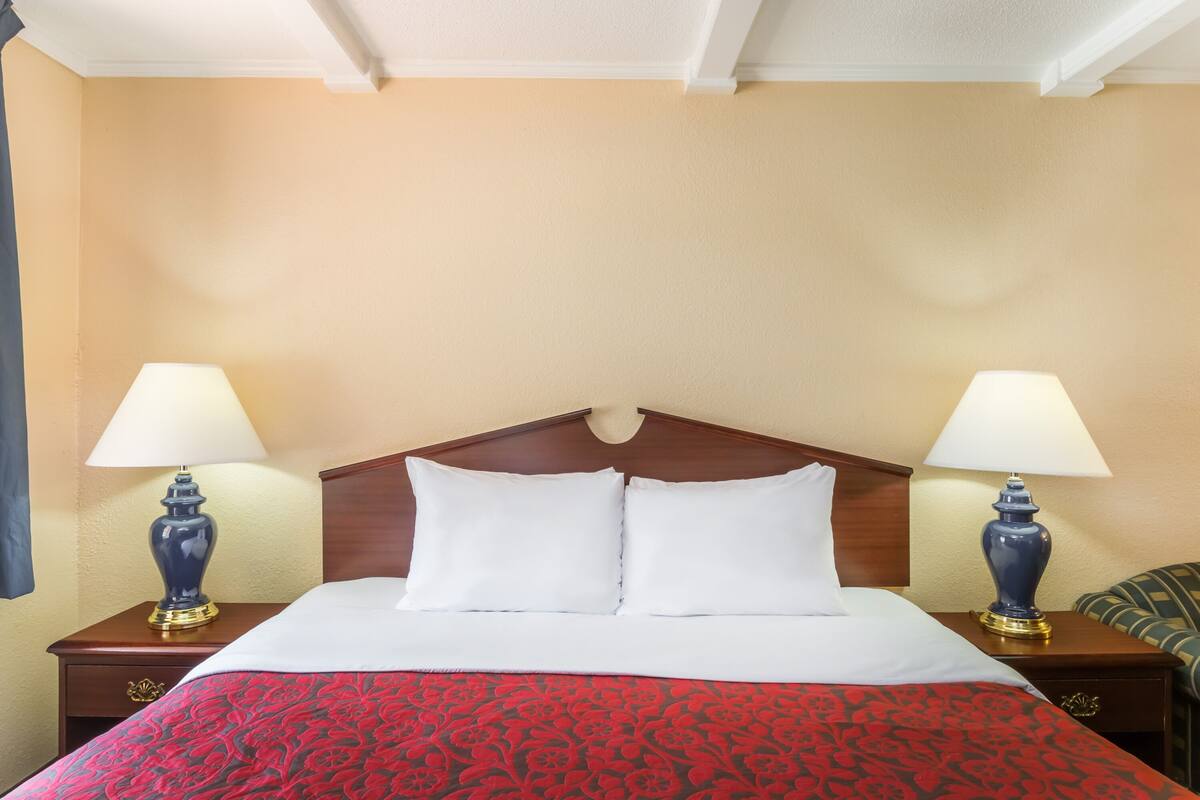 A neatly made bed with white linens and a red patterned bedspread, flanked by two wooden nightstands with lamps.