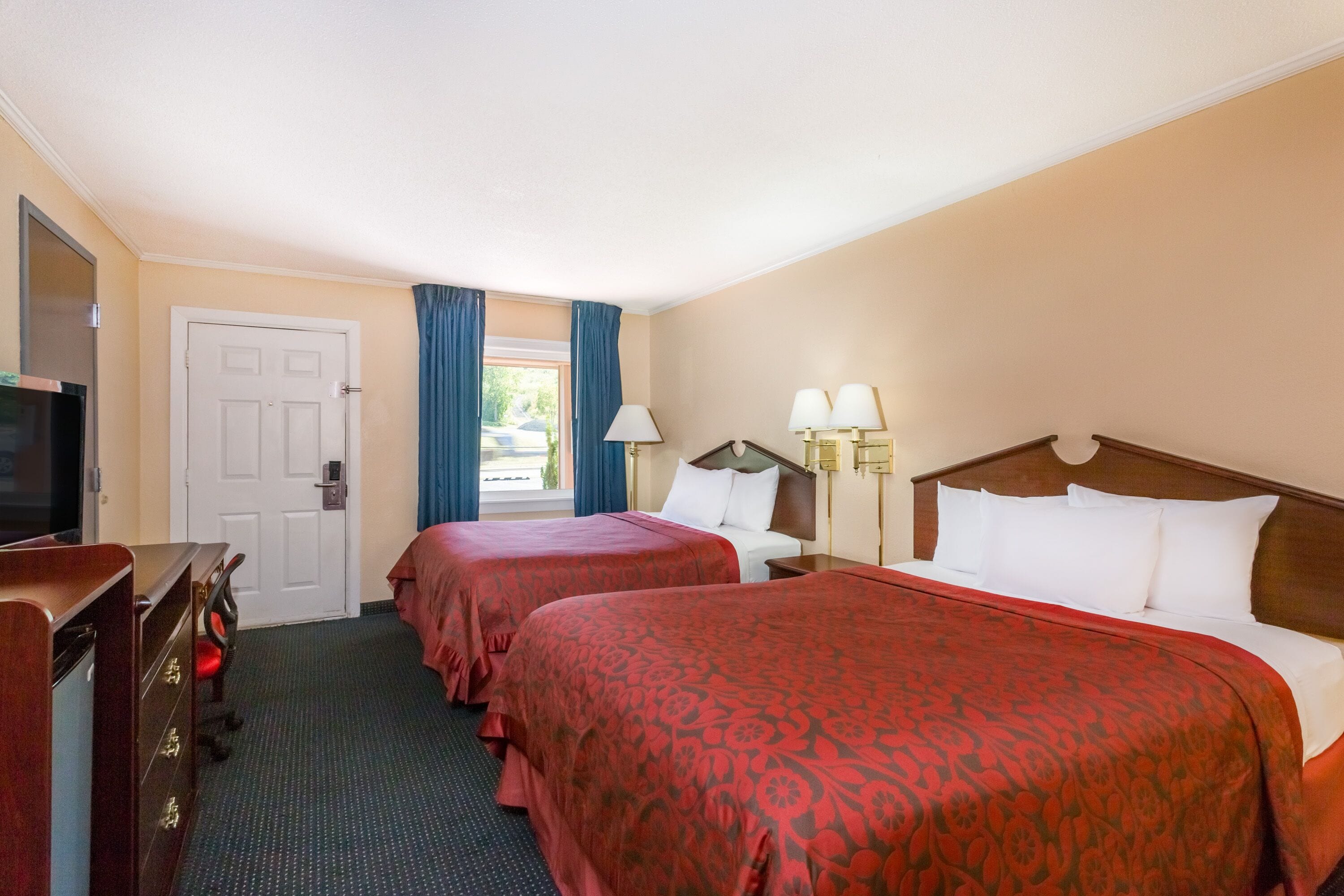 Een hotelkamer met twee bedden, een televisie, een bureau en een raam met gordijnen.