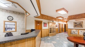 A reception area with a wooden reception desk, a clock, and a dining area with a table and chairs. - The Inn at Plantation (Jane Lew)