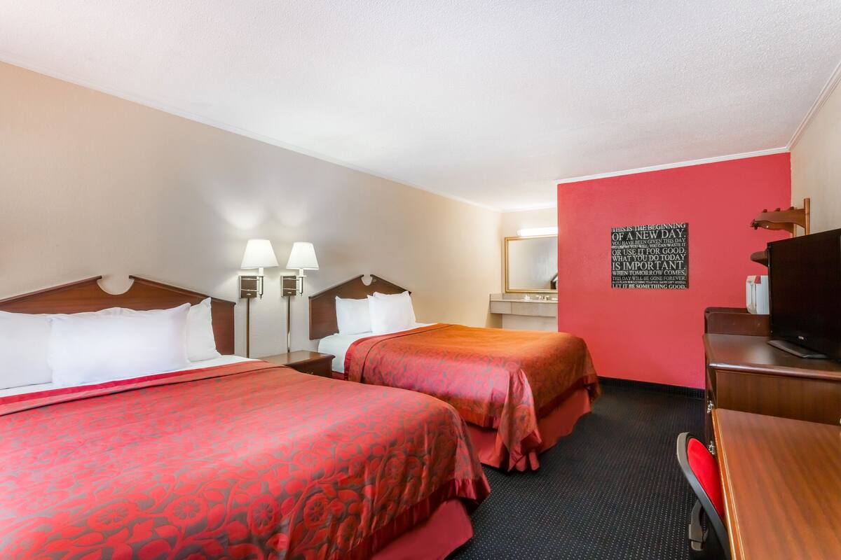 A hotel room with two beds, a desk, a chair, a TV, and a mirror.