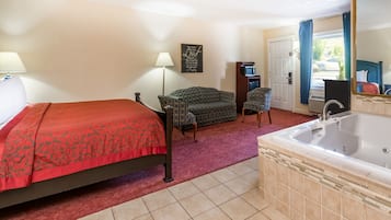 Habitación de hotel con cama, sofá, una mesita, una silla, baño con bañera y ventana con cortinas.
