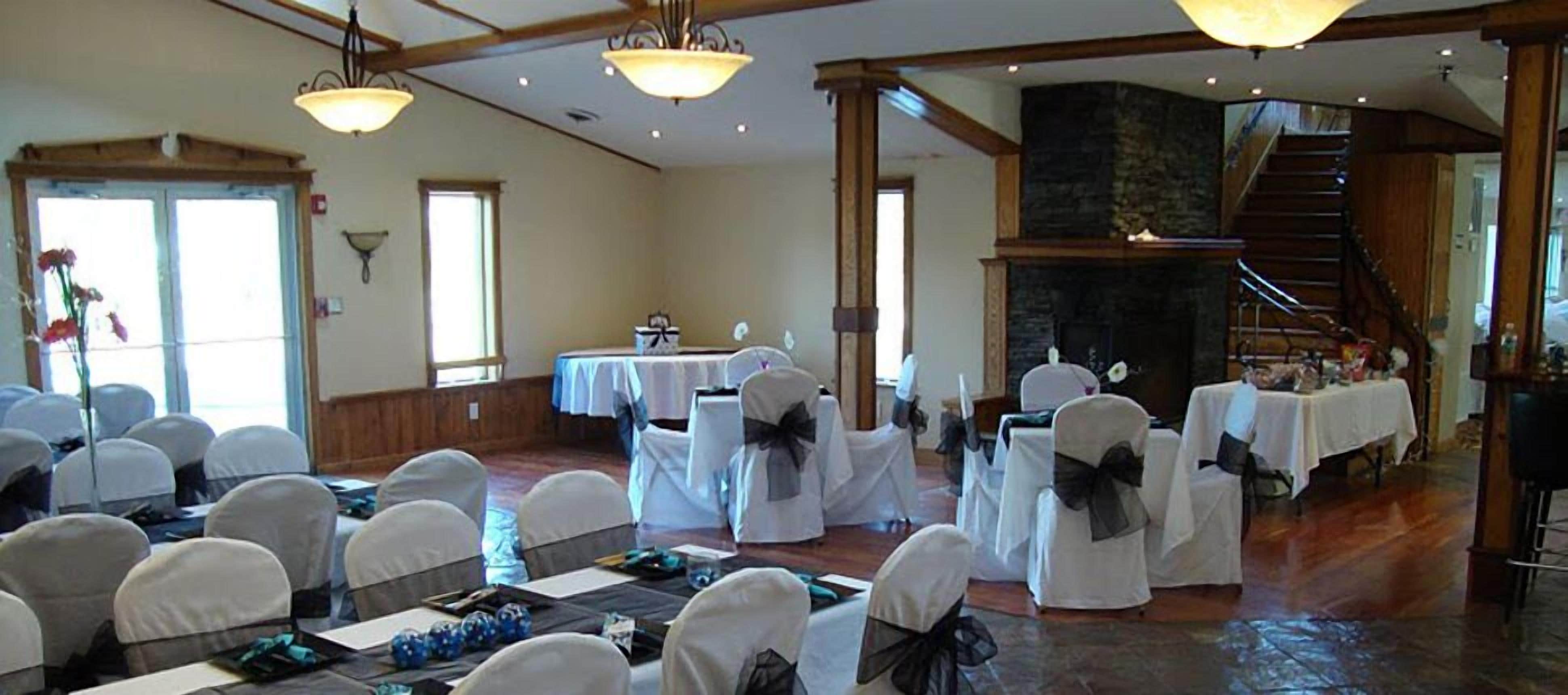 A banquet hall with round tables, white chairs, and a stone fireplace.