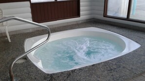 A spa area with a hot tub, a metal ladder, and a tiled floor. - Alpine Inn (Valemount)