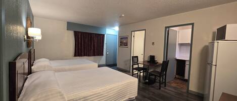 A hotel room with two beds, a desk with a chair, a refrigerator, and a microwave.