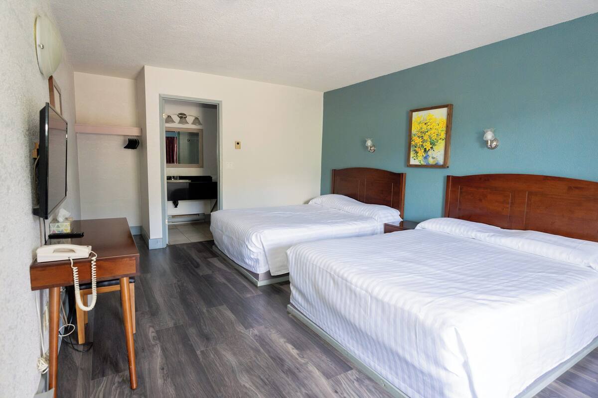 A hotel room with two beds, a desk with a telephone, a mirror, and a painting on the wall.