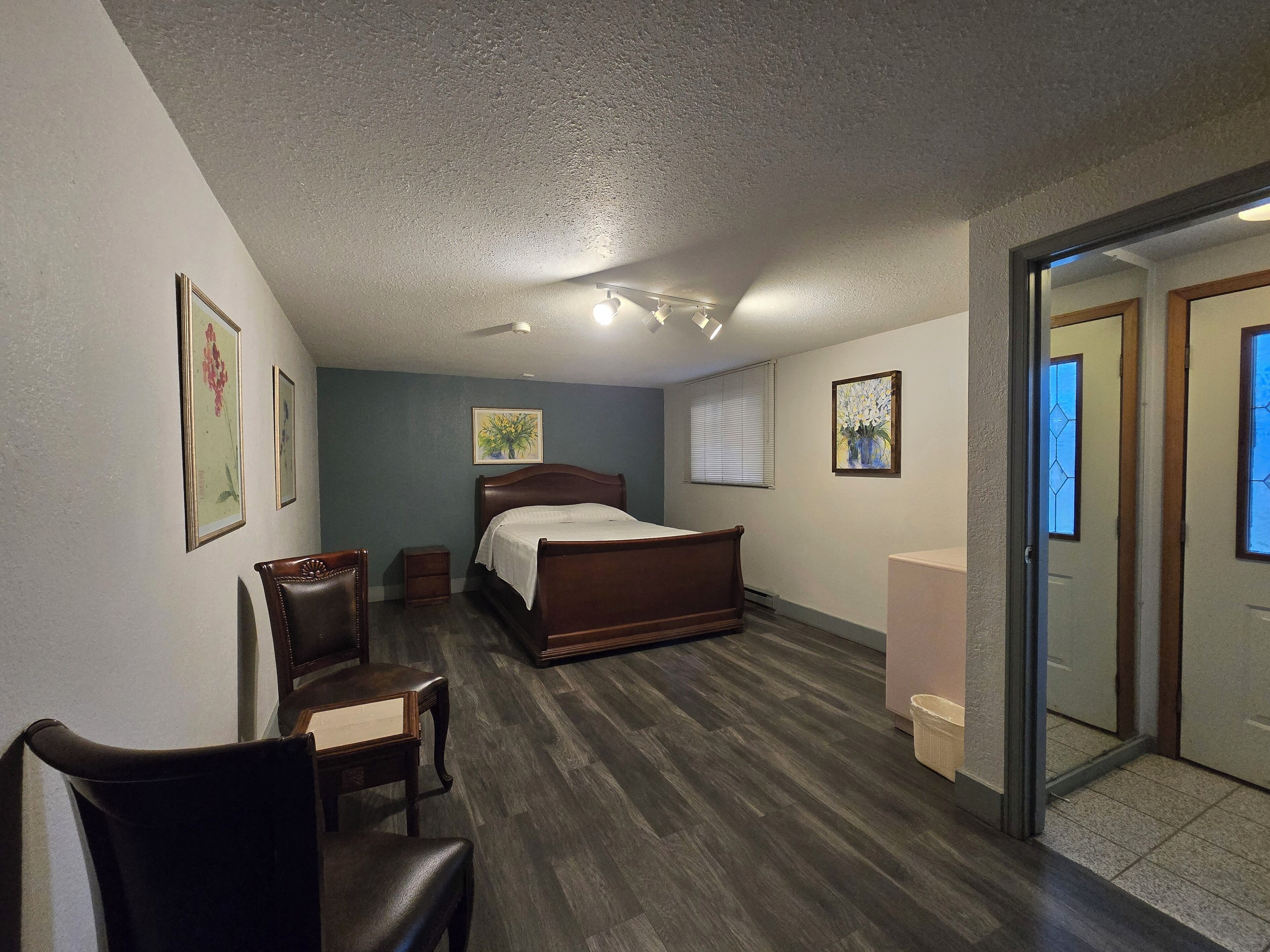 Un dormitorio con una cama de madera, una silla, una mesita y un ventanal con persianas.