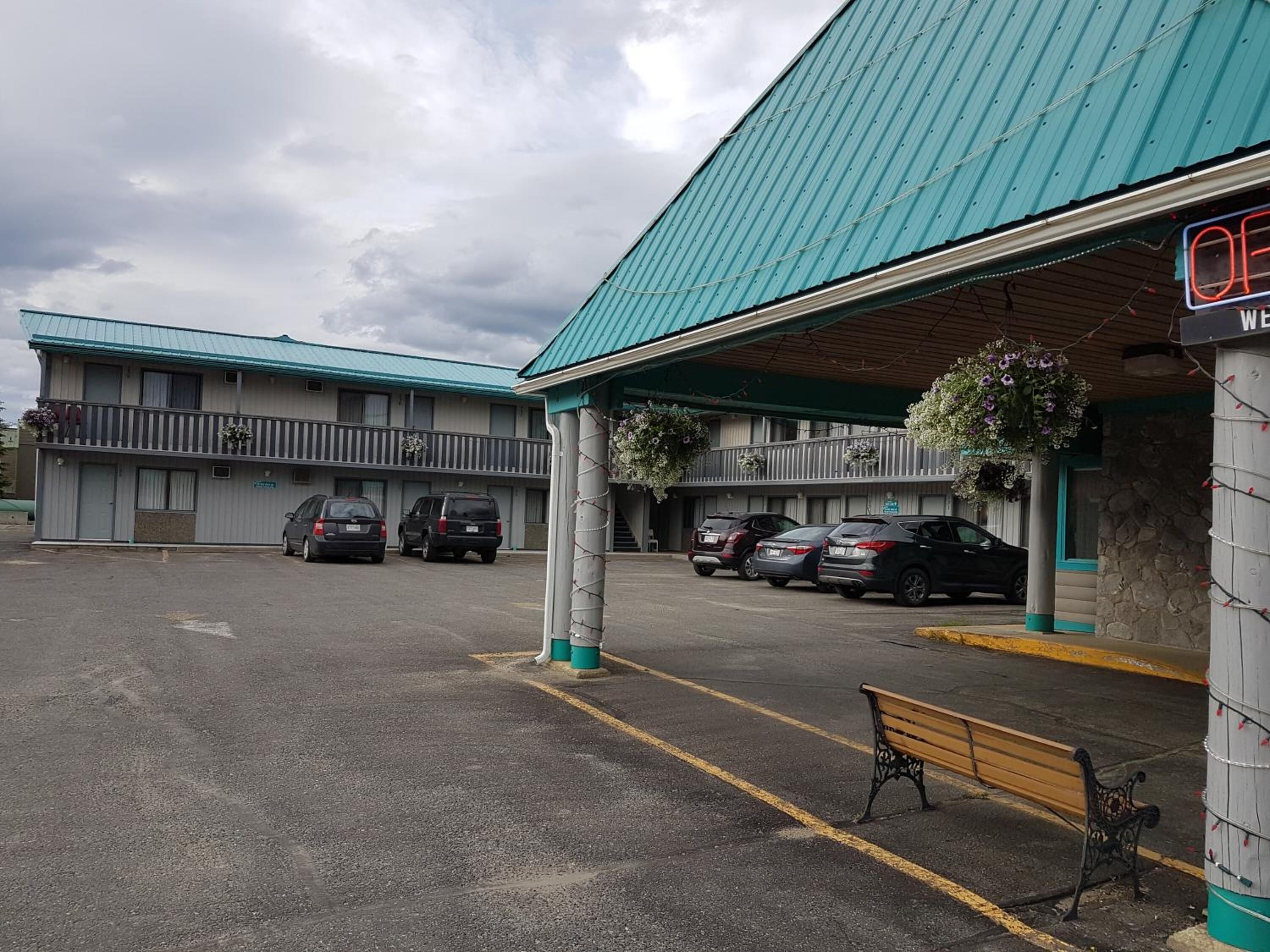 A motel with a green roof, a covered parking area, and several cars parked.
