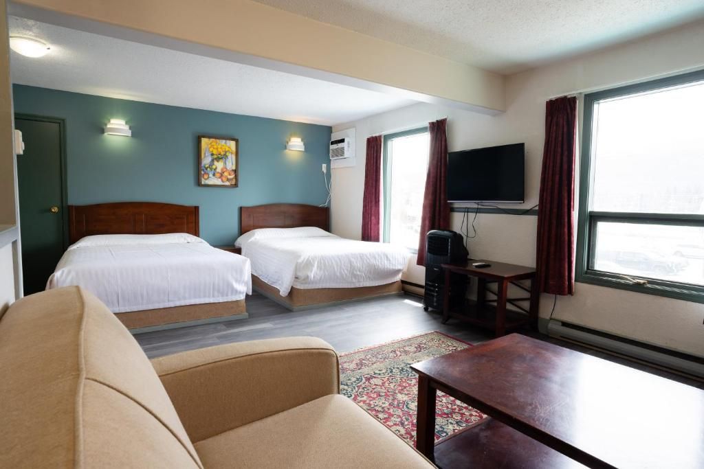 A hotel room with two beds, a television, a desk, and a window with curtains.