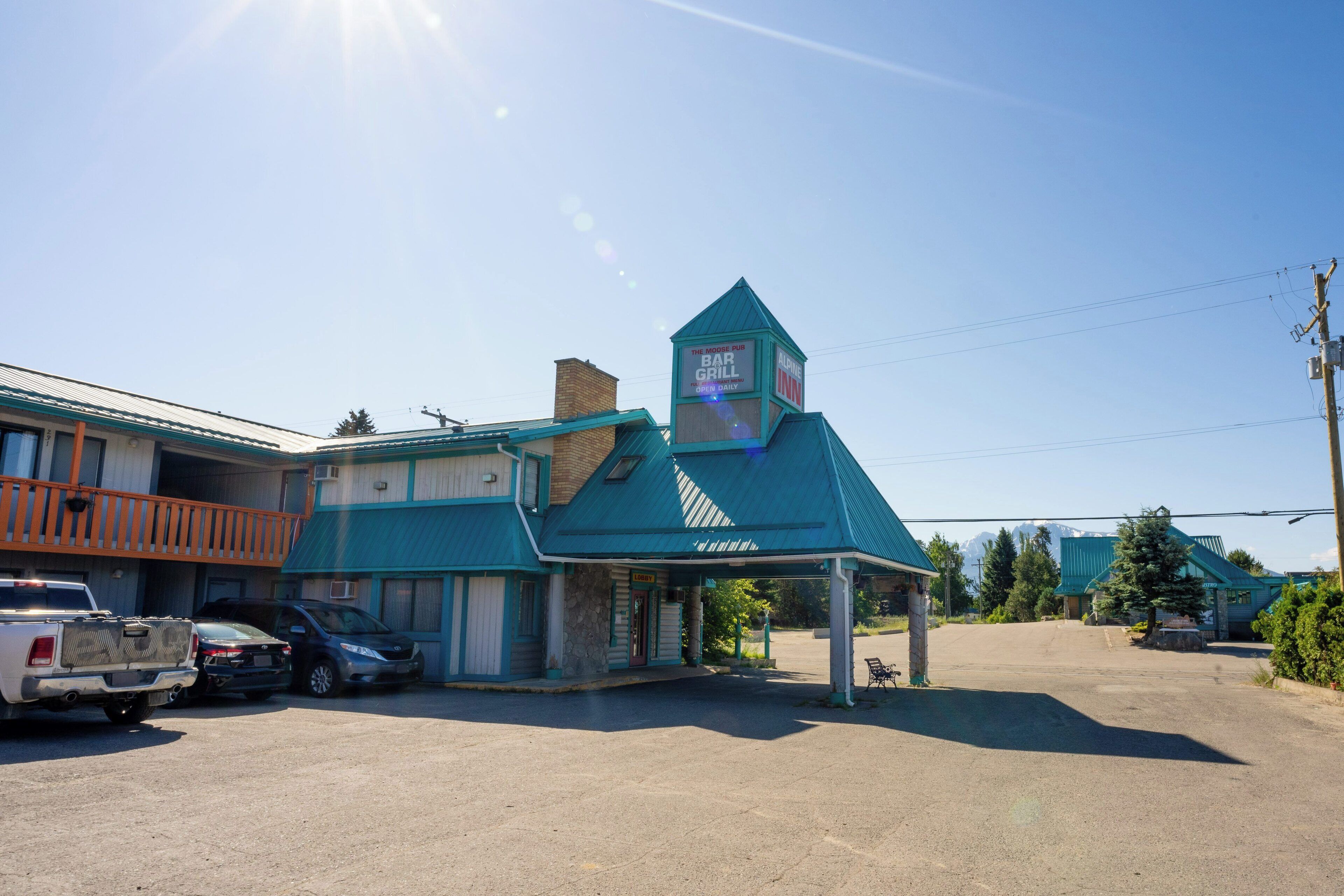 Un edificio con un letrero que dice 'The Bar Grill' y 'Alaska Inn', y un estacionamiento al frente.