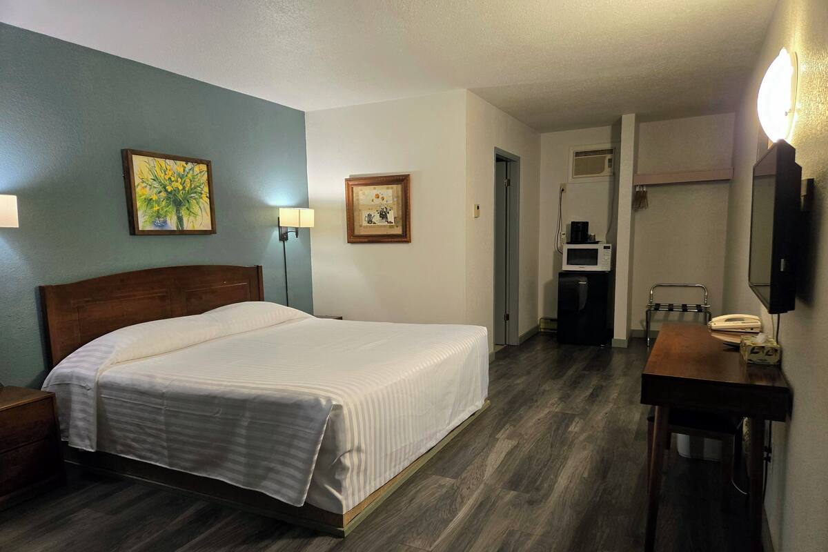 A hotel room with a bed, a desk with a telephone, a microwave, and a mirror.