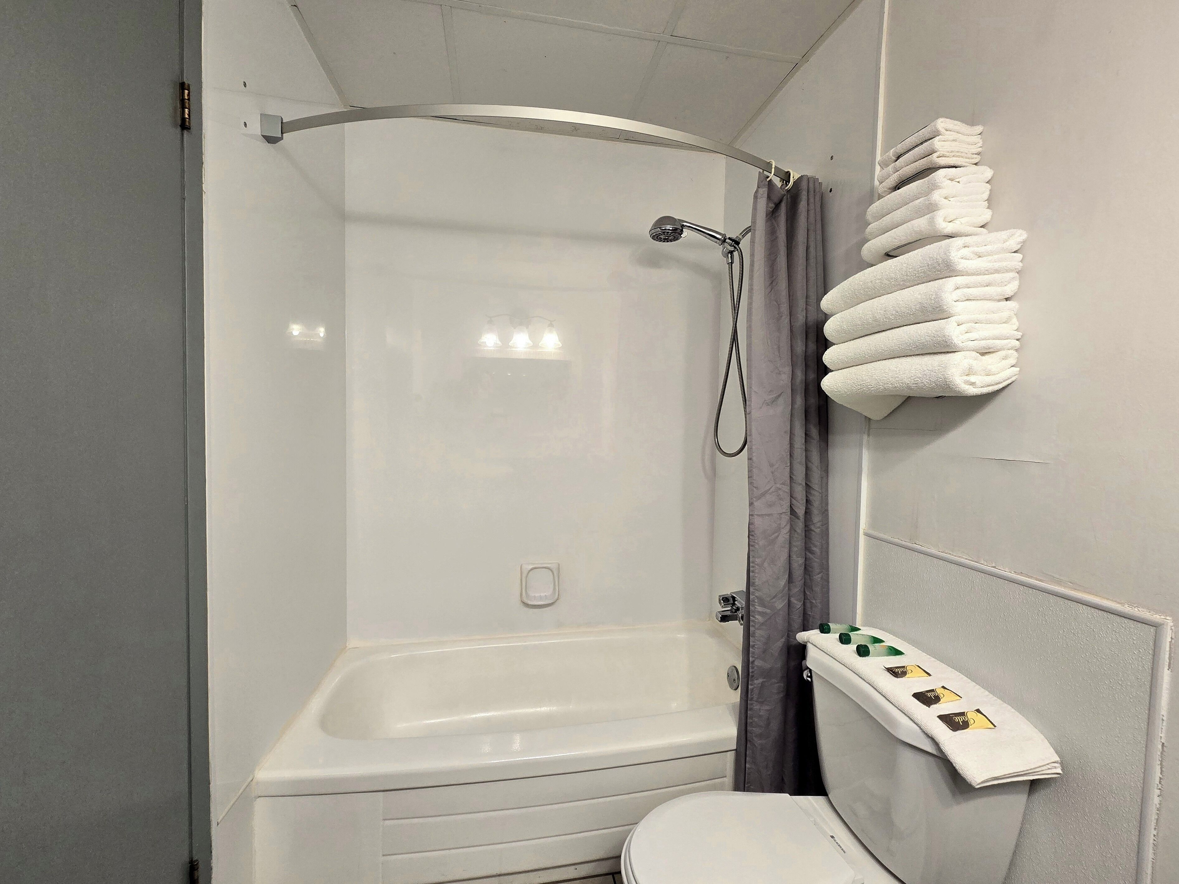 Un espacio de ducha con bañera, inodoro y un perchero con toallas dobladas.