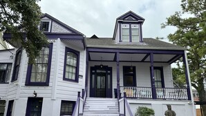 A two-story house with a front porch, a staircase, and a statue in the garden. - Oakview Bed and Breakfast (New Orleans)