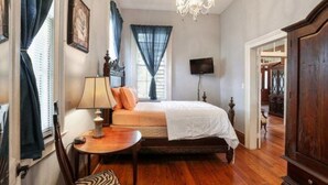 A bedroom with a bed, a desk, a chair, a chandelier, and a television. - Oakview Bed and Breakfast (New Orleans)