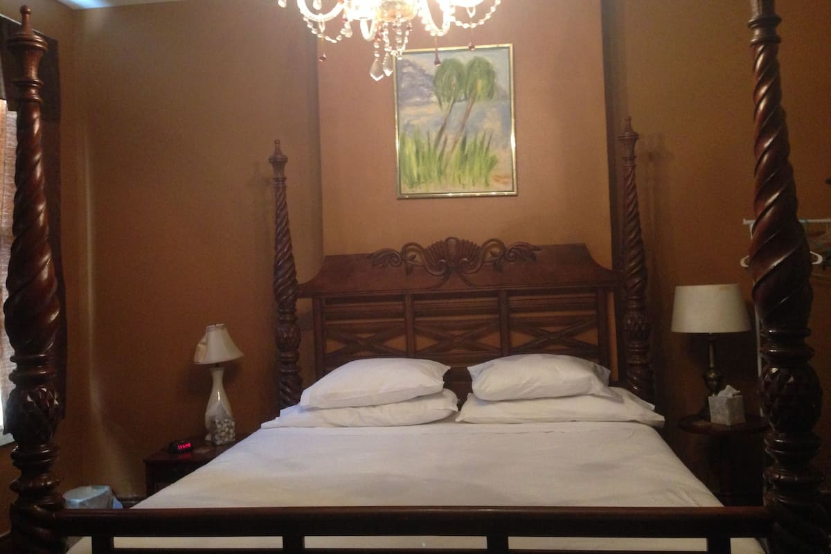 A four-poster bed with a wooden headboard, a chandelier, and a painting on the wall.