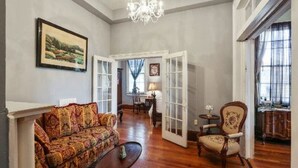 A spacious living room with a patterned sofa, a wooden coffee table, and a classic armchair. There is a chandelier, a painting on the wall, and a view through an open door. - Oakview Bed and Breakfast (New Orleans)