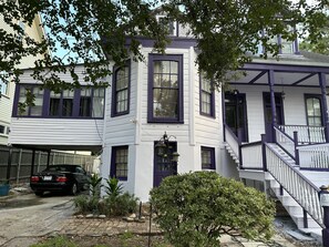 A two-story house with a white exterior and purple trim. There is a black car parked in the driveway, and a small garden with various plants and rocks. - Oakview Bed and Breakfast (New Orleans)