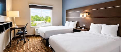 A hotel room with two beds, a desk with a lamp, a TV, and a window with a view of trees.