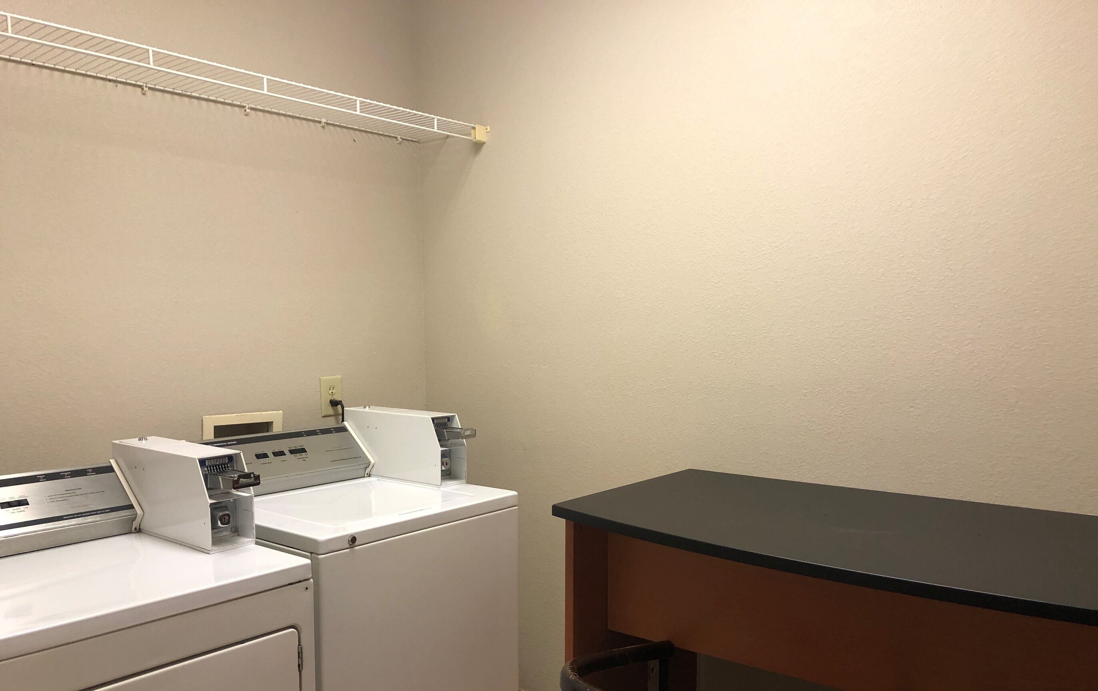 A laundry area with a washing machine and dryer, a shelf above the dryer, and a black countertop.