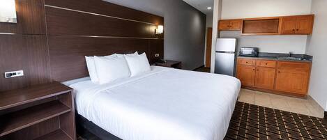 A hotel room with a large bed, a wooden headboard, a small kitchenette, and a patterned rug.