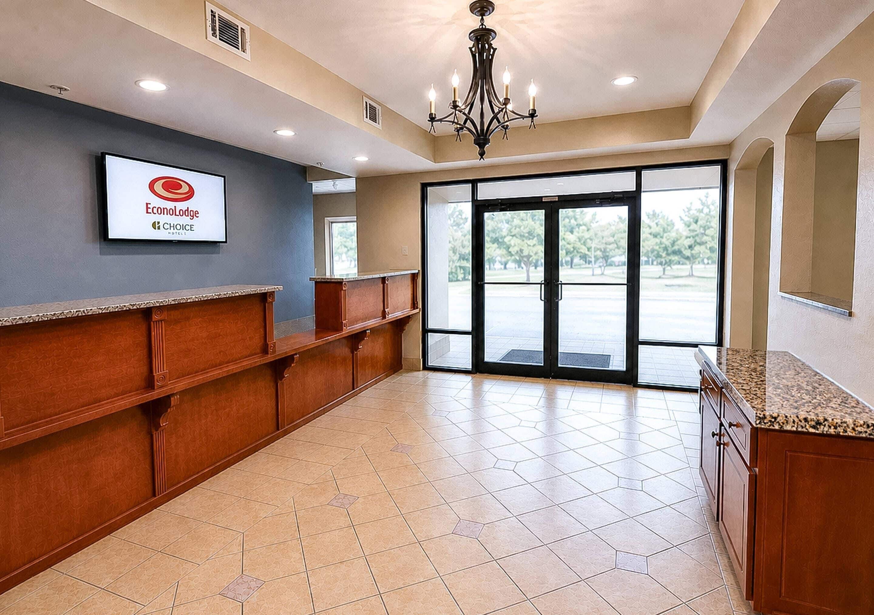 A hotel reception area with a reception desk, a chandelier, and a large glass door leading outside.