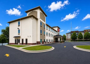 A multi-story hotel with a central entrance, a parking lot, and a clear blue sky.