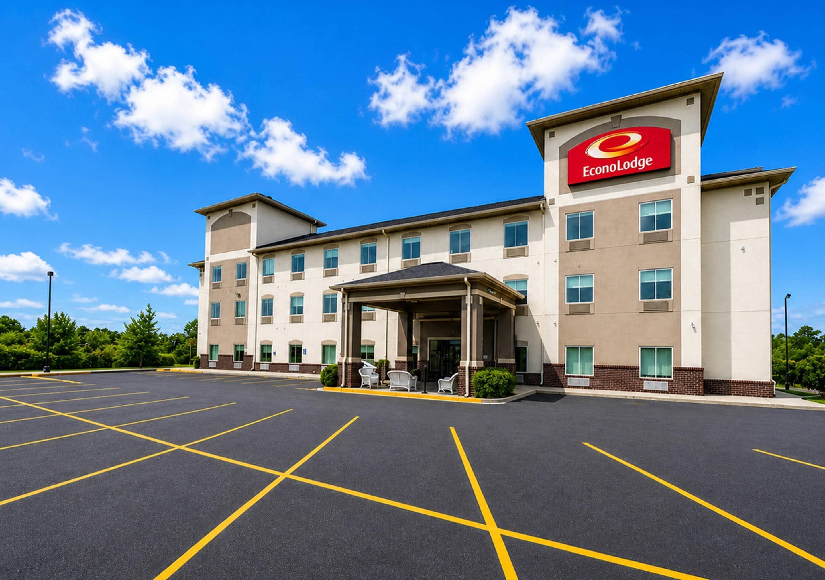 A hotel with a covered entrance, a parking lot, and a clear blue sky.