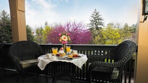 A balcony with wicker chairs, a table set with breakfast items, and a vase of flowers. - 1900 Inn on Montford (Asheville)