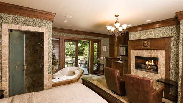 A spacious bedroom with a large bed, a fireplace, a jacuzzi, and a view of the outdoors. - 1900 Inn on Montford (Asheville)