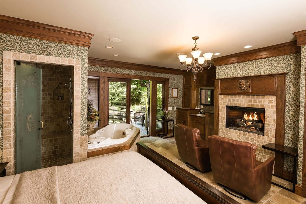 Un dormitorio amplio con una cama grande, una chimenea, un jacuzzi y vistas al exterior.