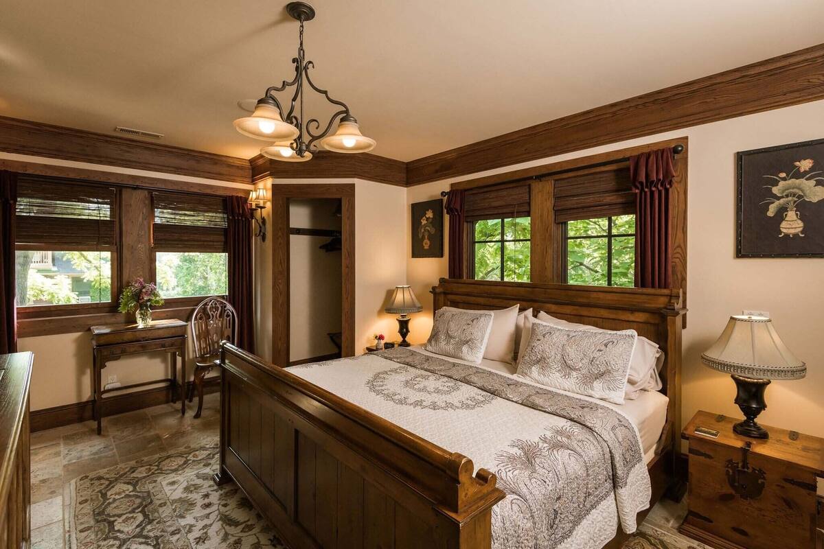 Un dormitorio tradicional con una cama de madera, un escritorio, una silla y una mesita de noche con lámpara.