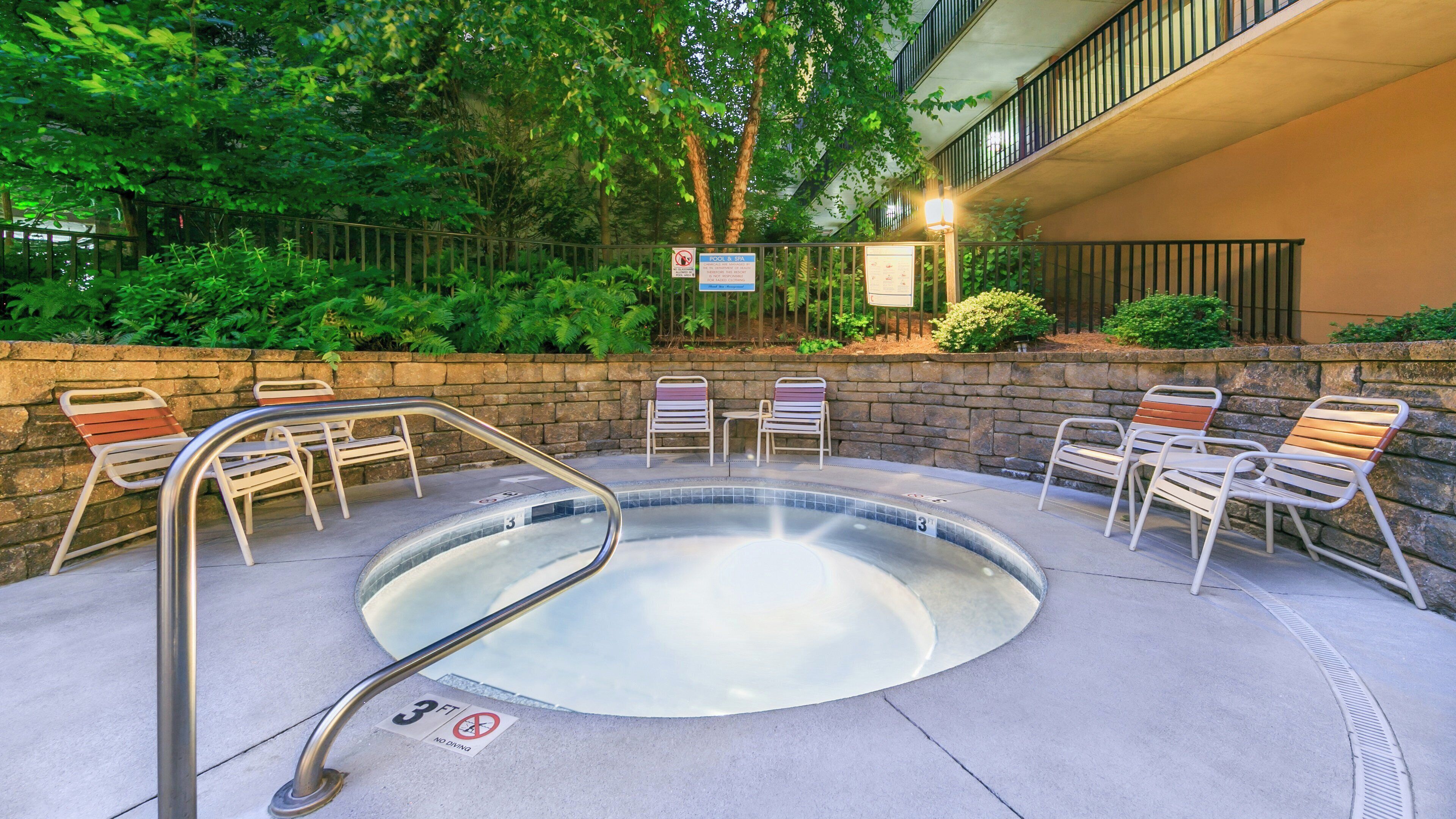 A hot tub area with a 3-foot no diving sign, surrounded by stone walls and metal chairs.