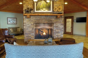Una sala de estar acogedora con chimenea de piedra, mobiliario de cuero y un televisor de pantalla plana montado en la pared.