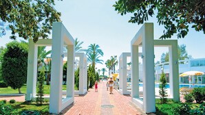 A paved pathway flanked by white columns, leading to a building with a blue and yellow exterior.