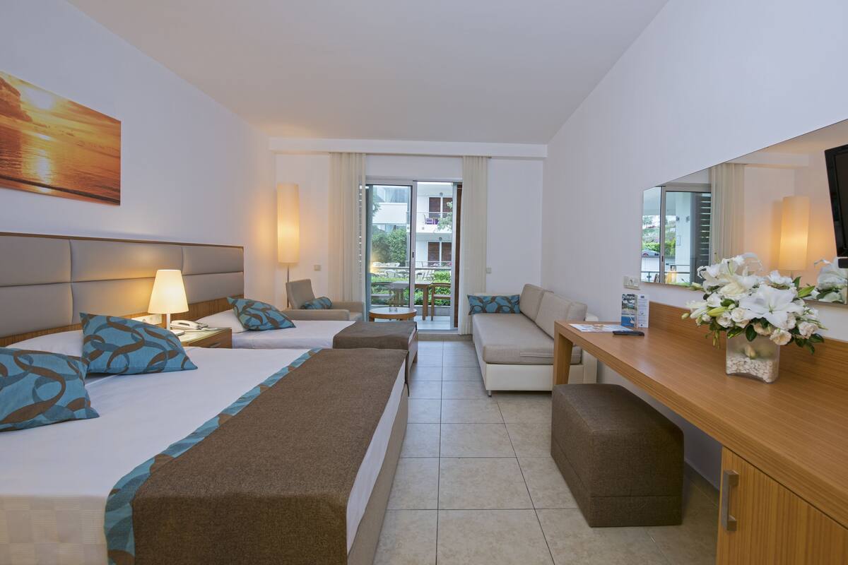 A hotel room with two beds, a sofa, a dining table, and a TV.