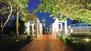 A paved pathway leading to a building with white pillars and a blue sky in the background.