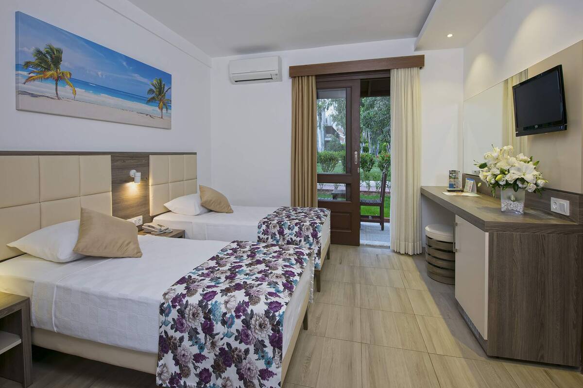 A hotel room with two beds, a desk, a TV, and a painting of a beach scene.