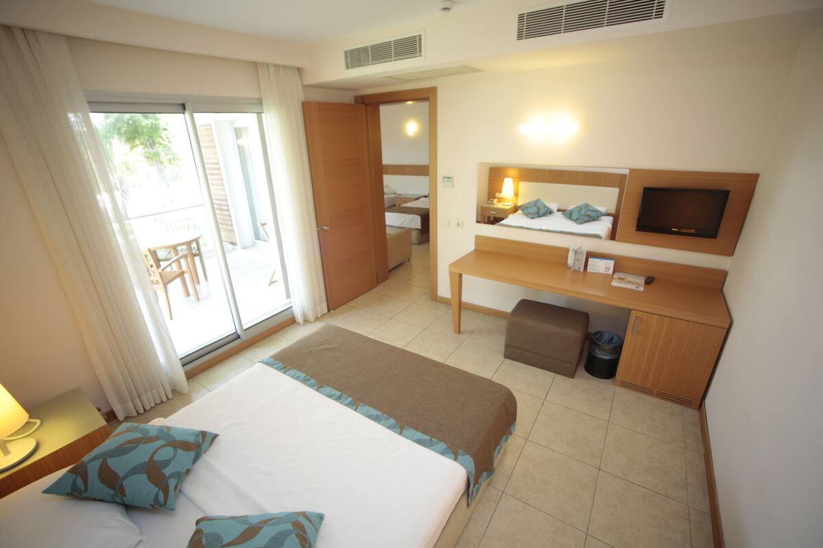 A hotel room with a large bed, a desk, a television, and a sliding door to a balcony.