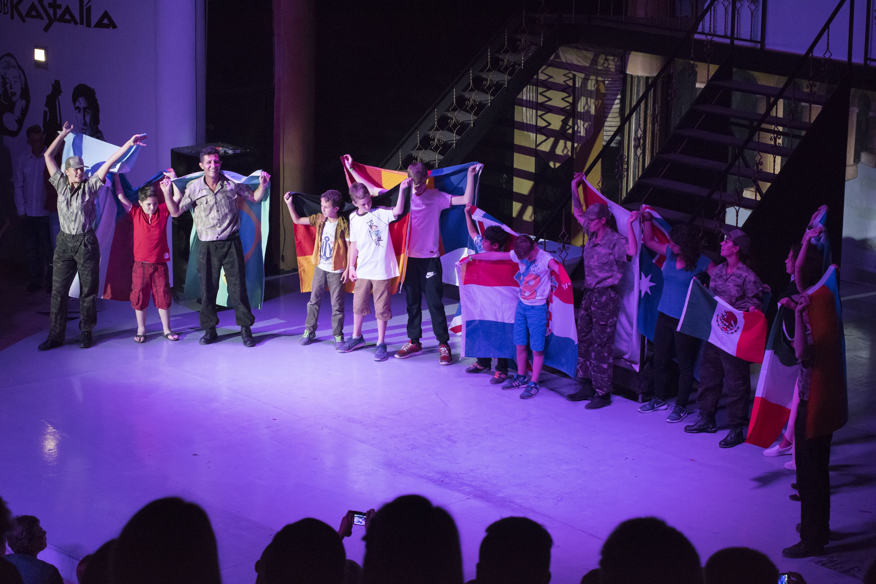 A group of people holding flags on a stage with a staircase in the background.