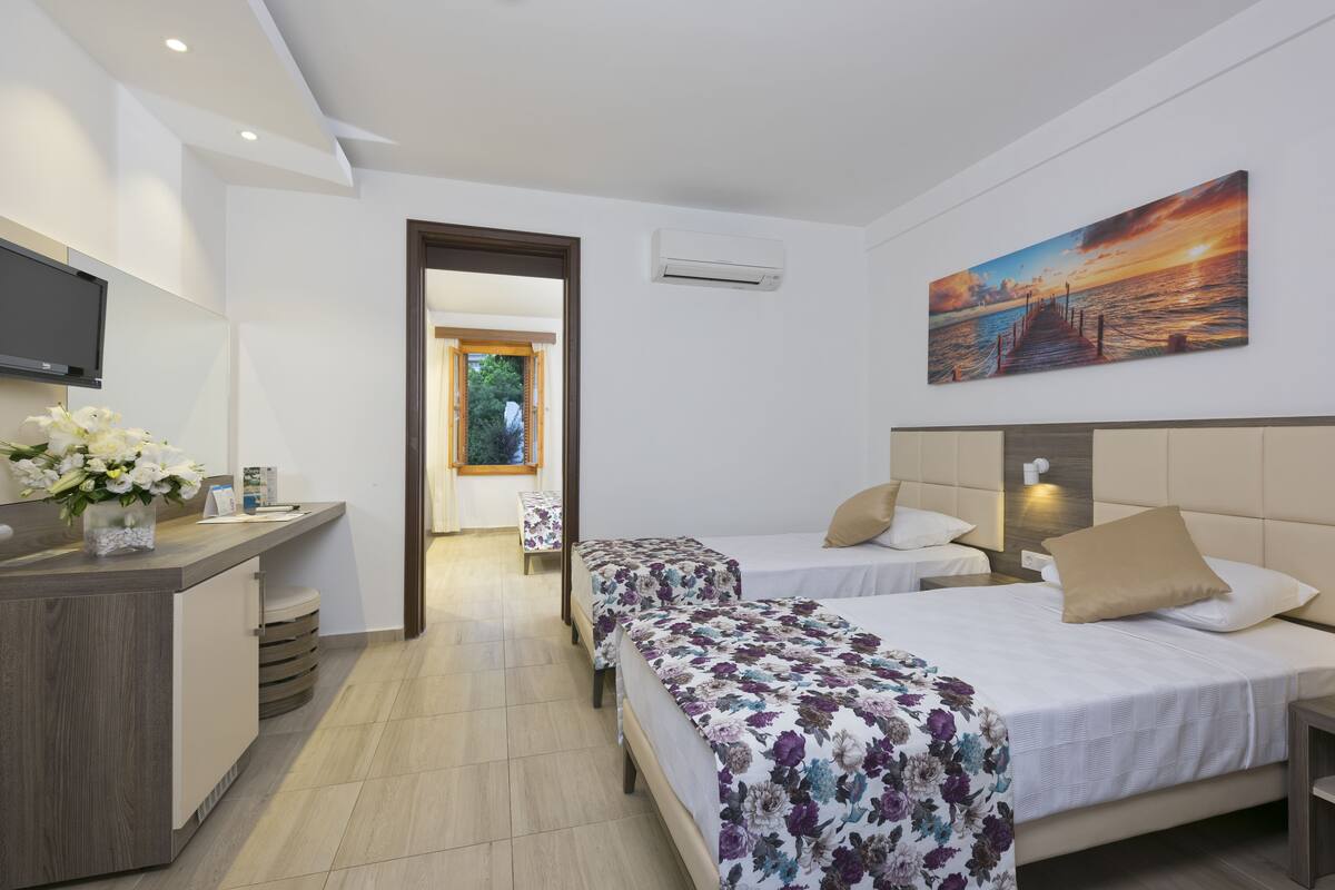 A hotel room with two beds, a desk, a TV, and a painting of a sunset.