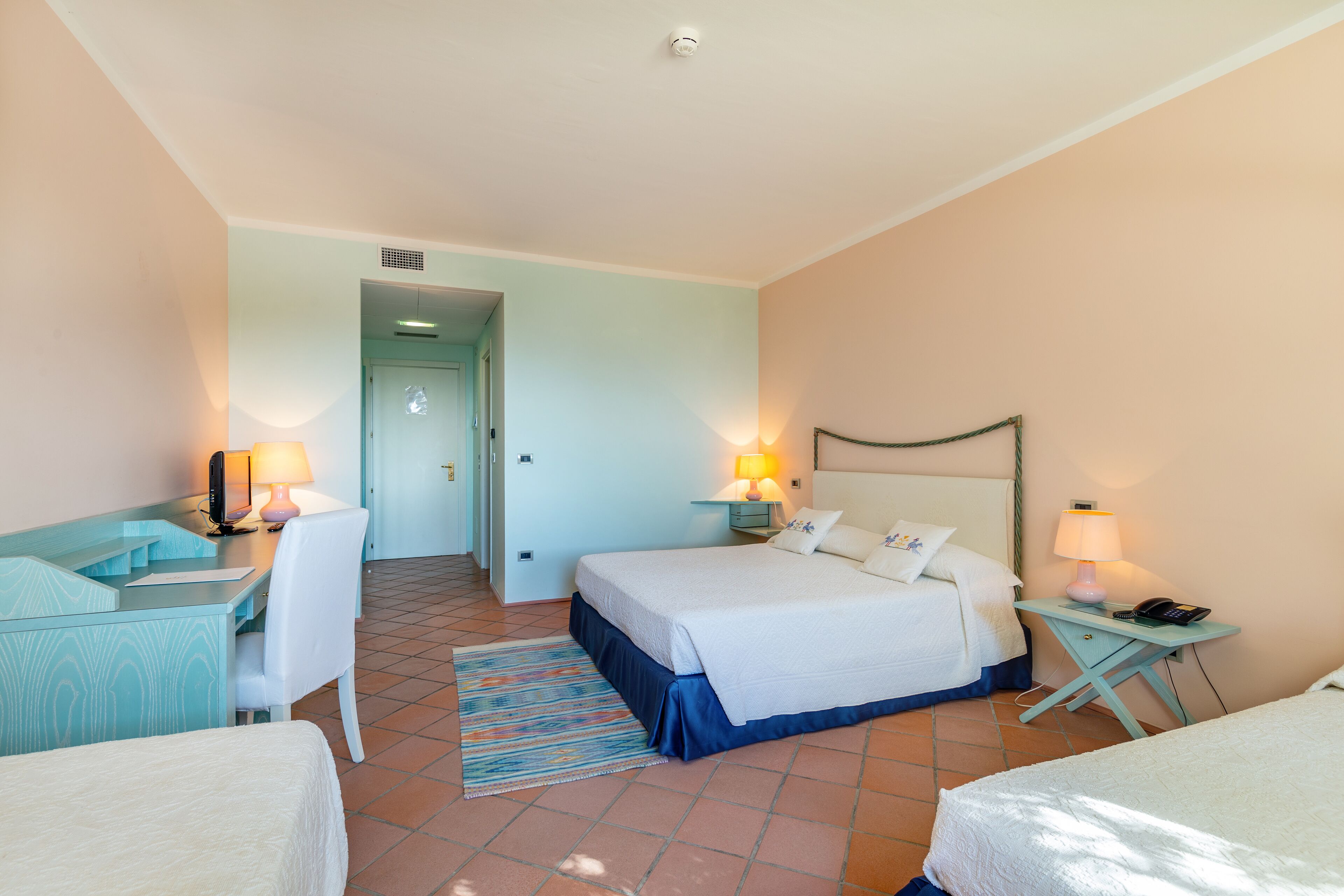 Une chambre d’hôtel comprenant un lit, un bureau, une chaise et deux tables de chevet avec des lampes.