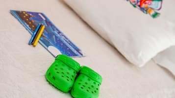 A white pillow with a colorful embroidered design, a pair of green slippers, and a blue card with a drawing.