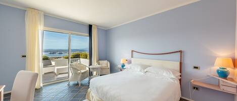 Una camera d'albergo con un letto grande, un balcone con vista, una sedia e un comodino con una lampada.