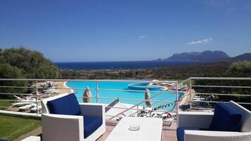 Una piscina al aire libre, sombrillas, sillones reclinables de piscina