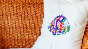 A wicker sofa with a white pillow featuring a colorful fish design, and a vibrant abstract painting on the wall.