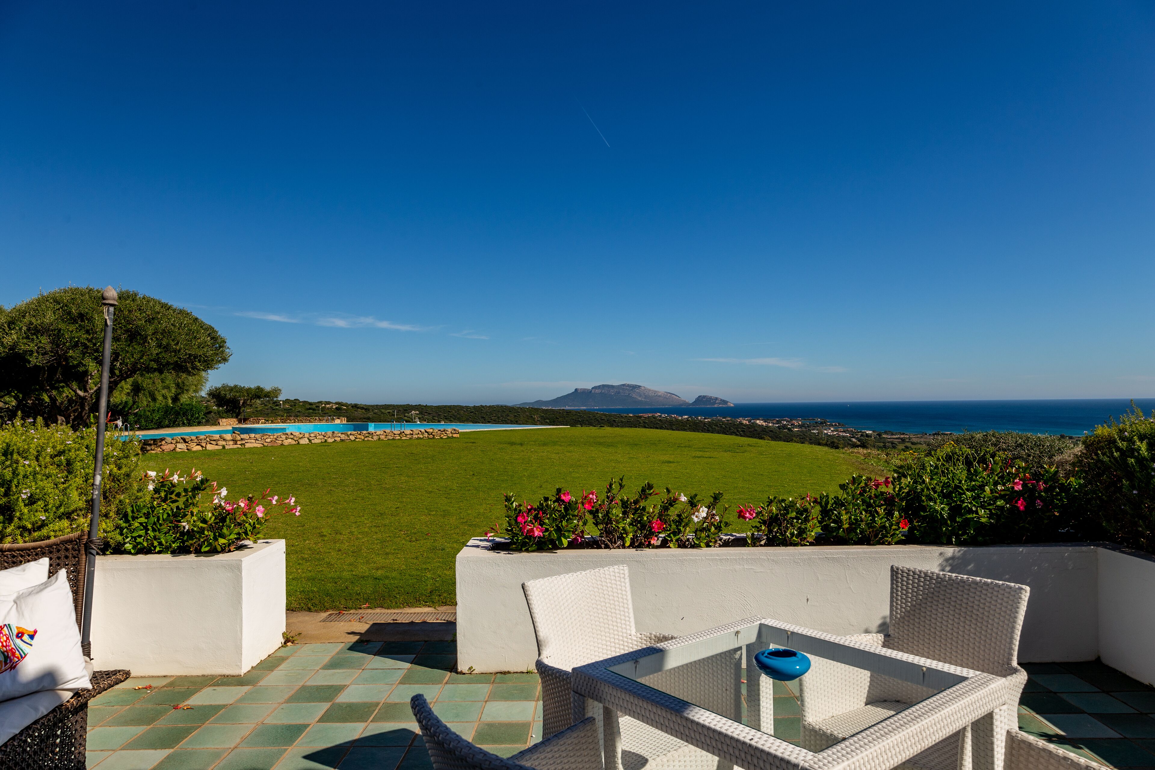 A patio with a view of the ocean, a pool, and a grassy area.