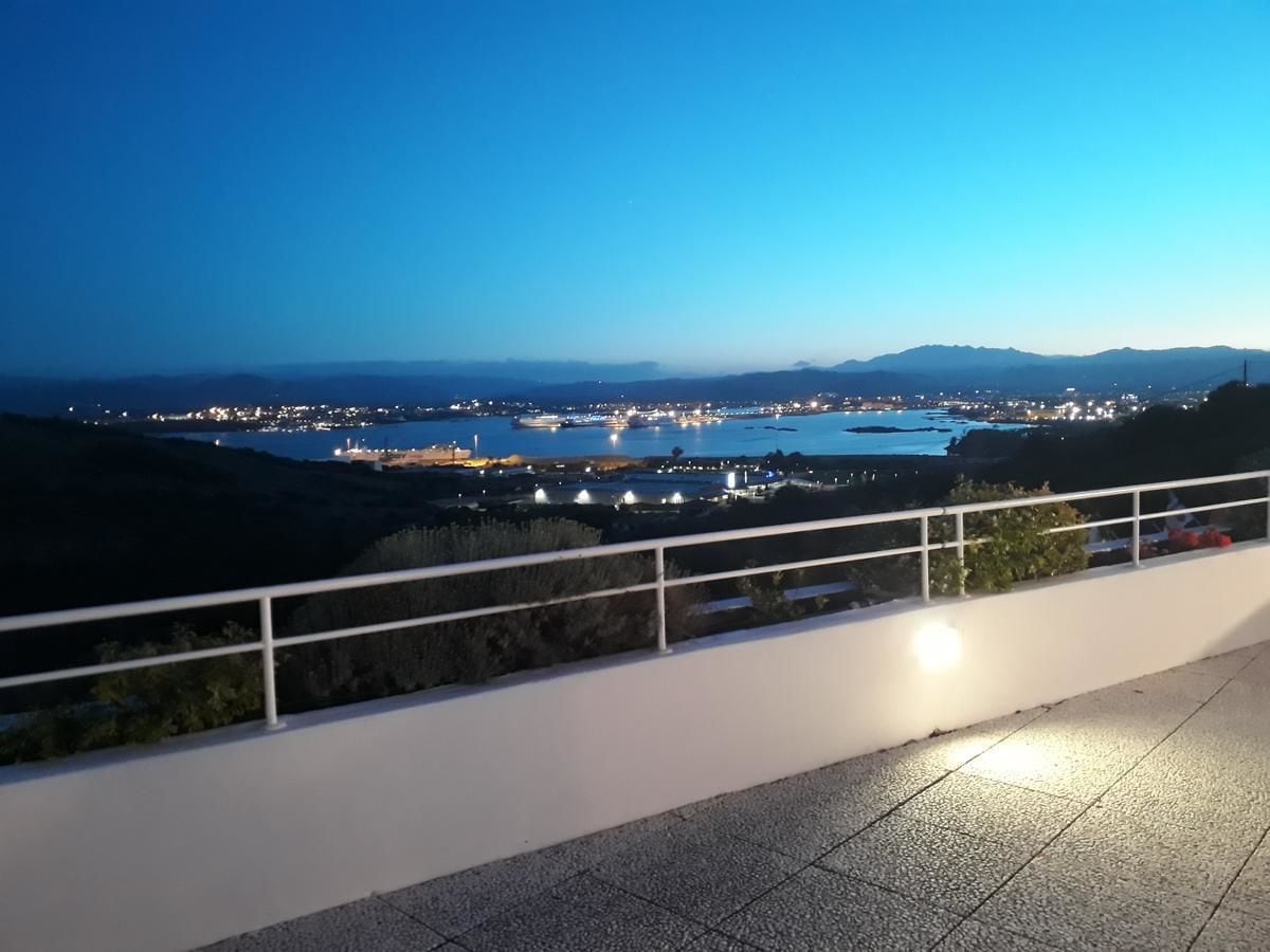 Nachtansicht von einem Balkon mit Blick auf eine Küstenstadt, in der Ferne Berge und ein Gewässer.