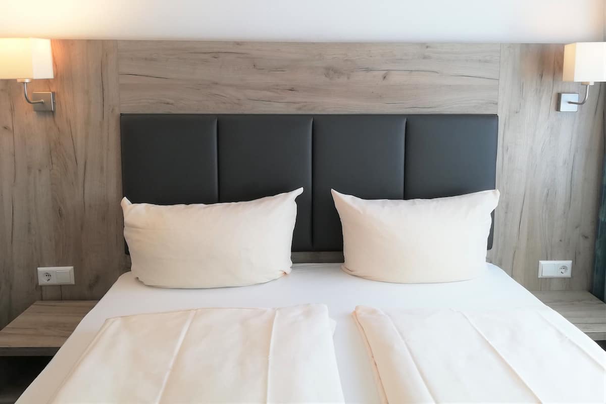 A bed with a dark headboard, two white pillows, and a white bedspread.